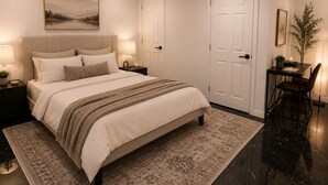 A bedroom with a large bed, bedside lamps, a rug, a desk with a chair, and a door.