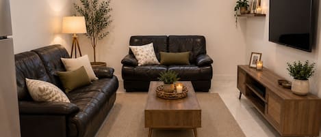 A modern living room with a leather sofa, a wooden coffee table, and a TV mounted on the wall.