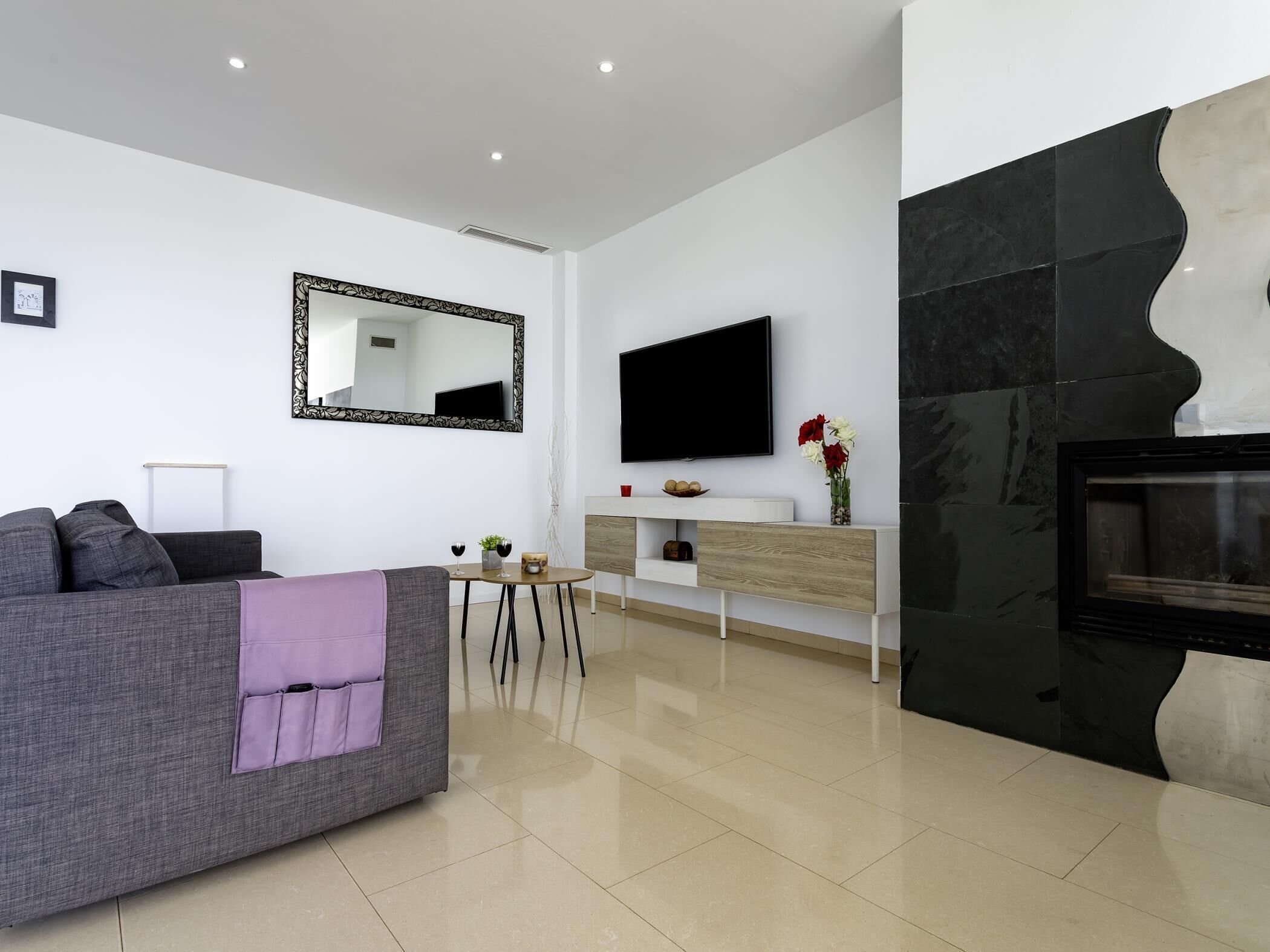 A modern living room with a sofa, a coffee table, a flat-screen TV, and a fireplace.