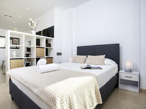 A modern bedroom with a large bed, a white wardrobe, and a bedside table with a lamp. - Sunstay Flat Caribe. (Benalmádena)