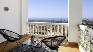 Ein Balkon mit Meerblick, zwei Stühle, ein Tisch und eine kleine Pflanze.