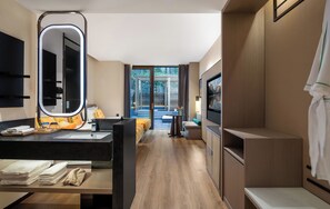 A modern hotel room with a large mirror, a bed with colorful bedding, a TV, and a view of a garden through the door. - Yinmo Hotel (Chongqing)