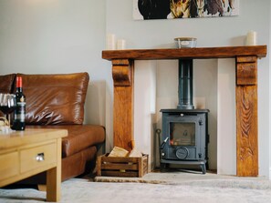 Ein Wohnzimmer mit braunem Ledersofa, einem Holztisch mit einer Weinflasche, einem Kaminofen und einem Kaminumbau mit Kerzen.