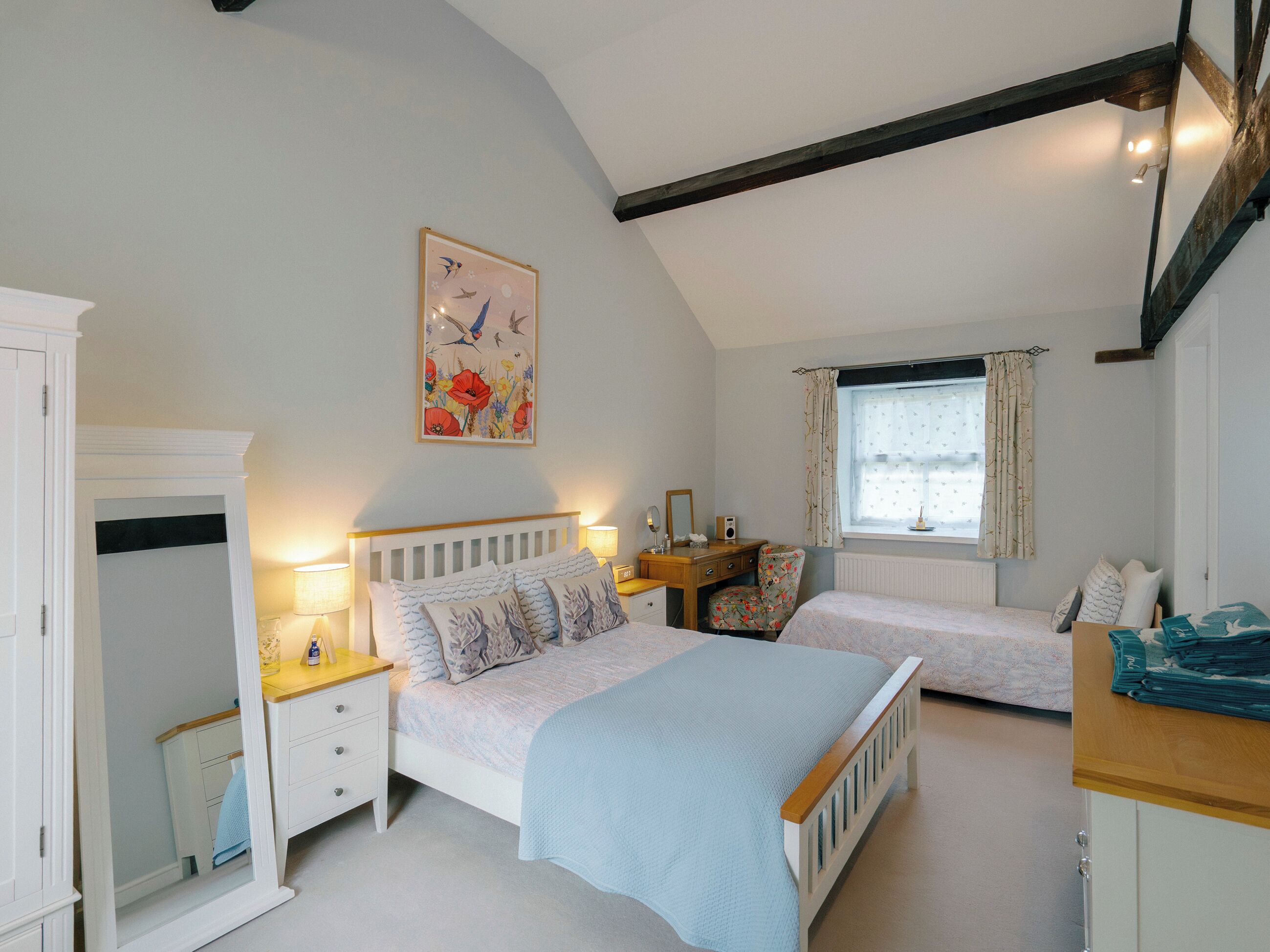 Un dormitorio con dos camas individuales, un aparador, un tocador y una ventana con cortinas.