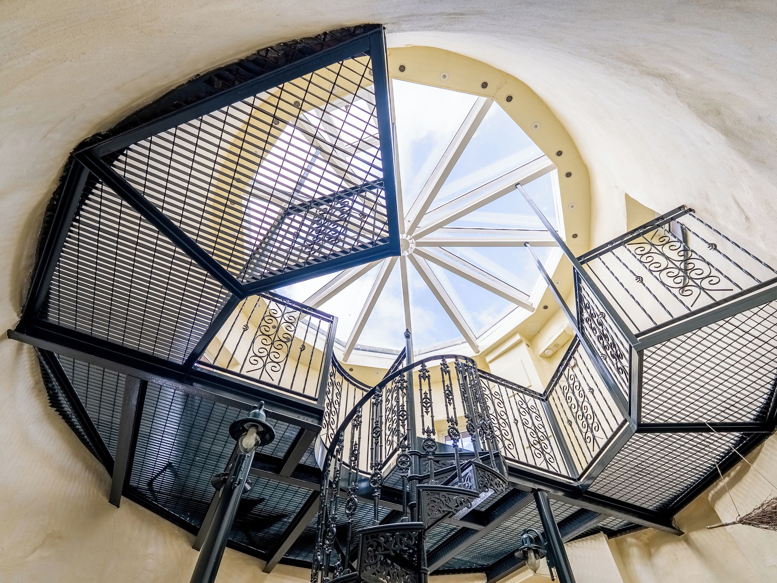 Un escalier en colimaçon orné de rampes en métal ouvragé et surmonté d’une lucarne.