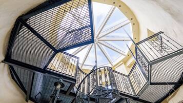 Un escalier en colimaçon orné de rampes en métal ouvragé et surmonté d’une lucarne.