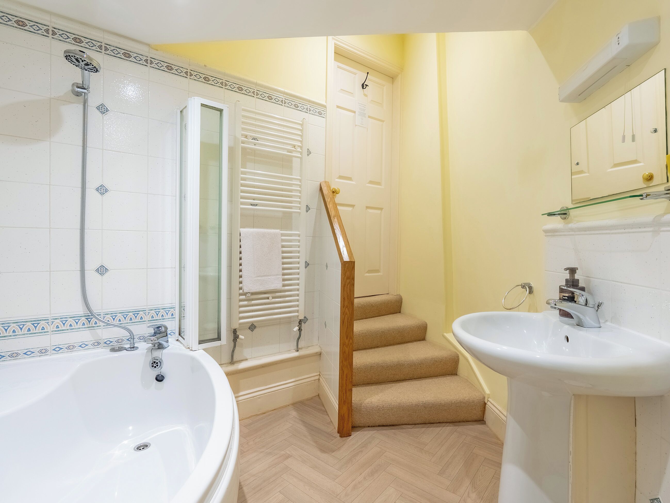 Een badkamer met een bad, een douche, een wastafel en een houten trap naar een deur.