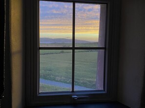 A window with a view of a landscape, including a field and distant hills.