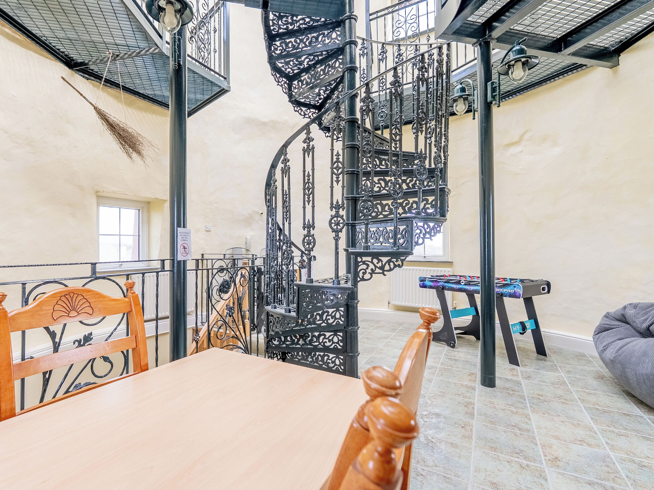 A spiral staircase with ornate metal railings, a wooden table with a chair, and a bench in a room with tiled flooring.