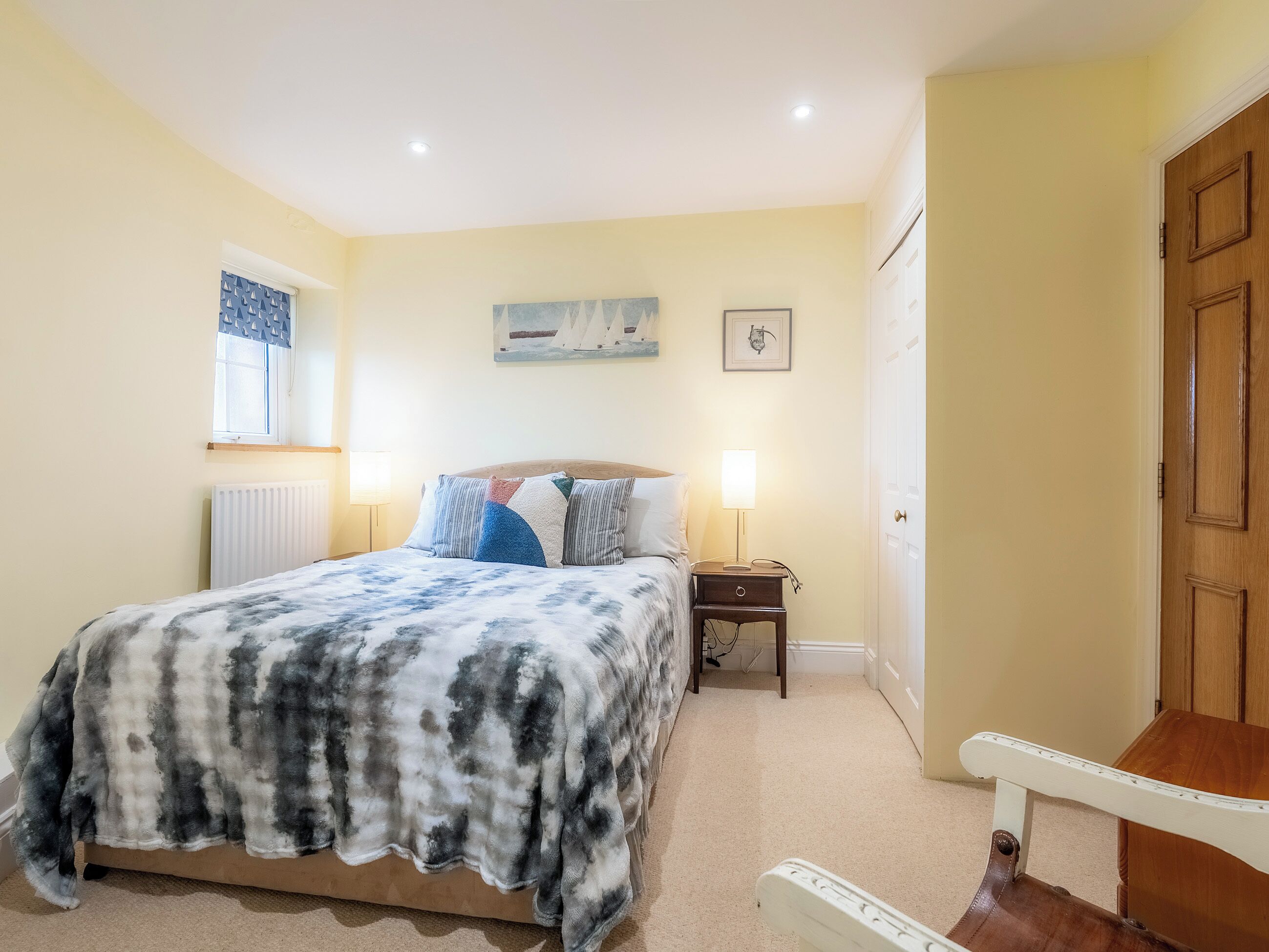 A bedroom with a bed, bedside lamps, a window with curtains, a door, and a small table.