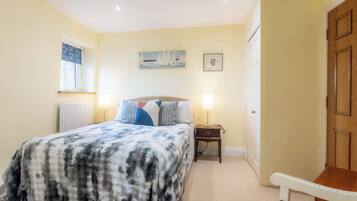 A bedroom with a bed, bedside lamps, a window with curtains, a door, and a small table.