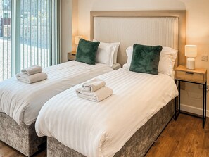 A hotel room with two beds, each with a pillow and a folded towel. There is a nightstand with a lamp and a wooden side table with a lamp. - 5 bedroom accommodation in Auchtermuchty (Auchtermuchty)