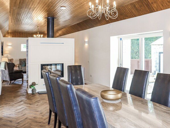 A dining area with a wooden herringbone floor, a central table with chairs, a chandelier, and a fireplace.
