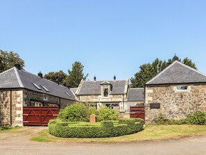 A stone building with a red gate, a well-maintained hedge, and a clear blue sky.