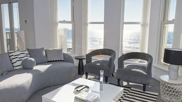 Un salon moderne avec un canapé, des fauteuils, une table basse et de grandes fenêtres donnant sur la mer.