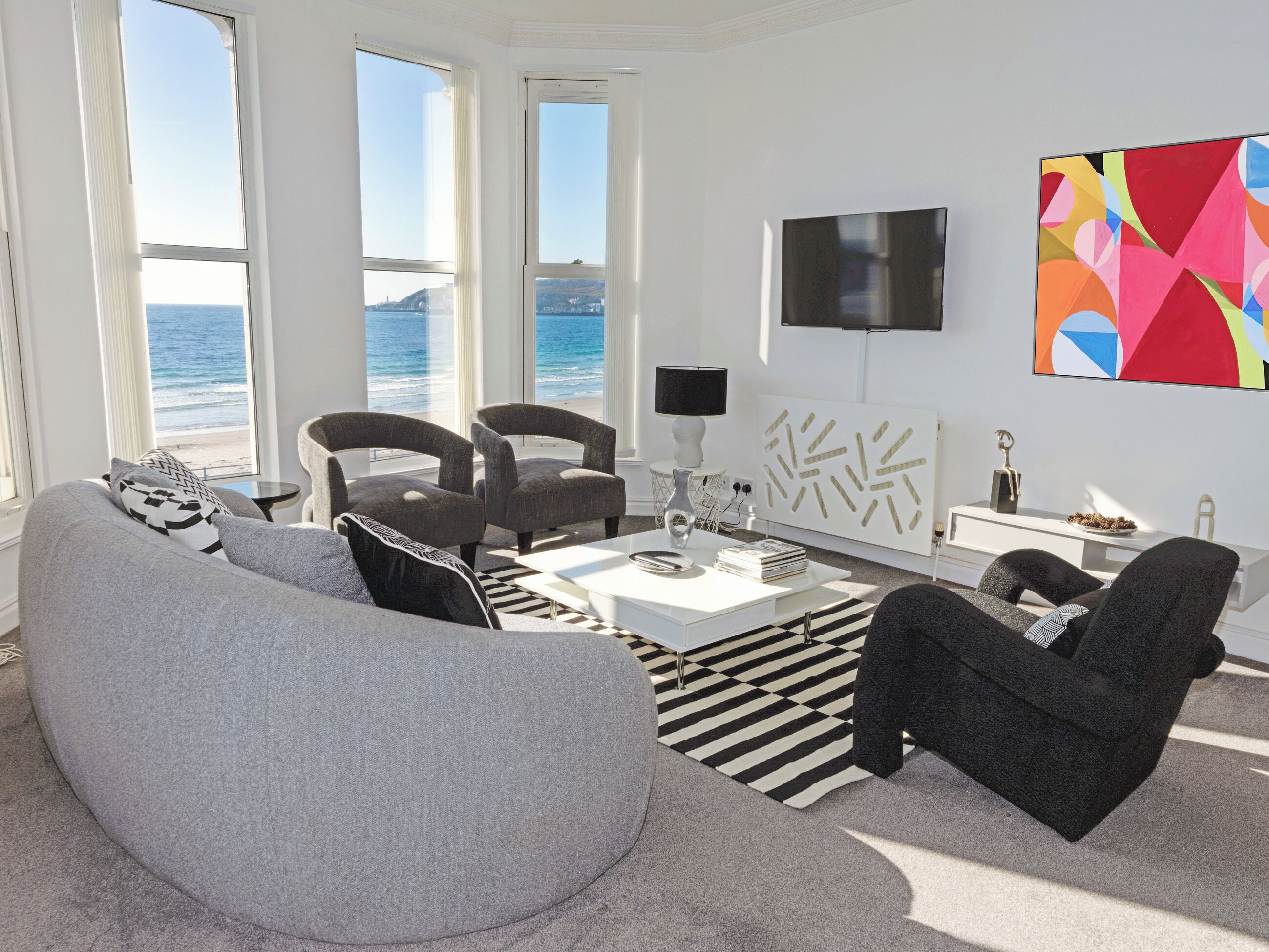A modern living room with a sofa, armchairs, a coffee table, and a view of the ocean.