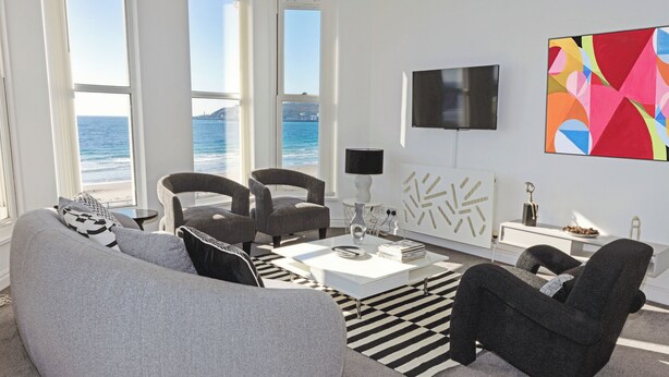 A modern living room with a sofa, armchairs, a coffee table, and a view of the ocean.