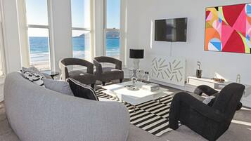 A modern living room with a sofa, armchairs, a coffee table, and a view of the ocean.