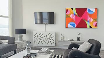 A modern living room with a flat-screen TV, abstract art, a patterned cabinet, and a coffee table with books and decorative items.