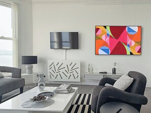A modern living room with a flat-screen TV, abstract art, a patterned cabinet, and a coffee table with books and decorative items.
