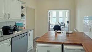 A modern kitchen with white cabinetry, a wooden countertop, and a view to a living area through an open door.