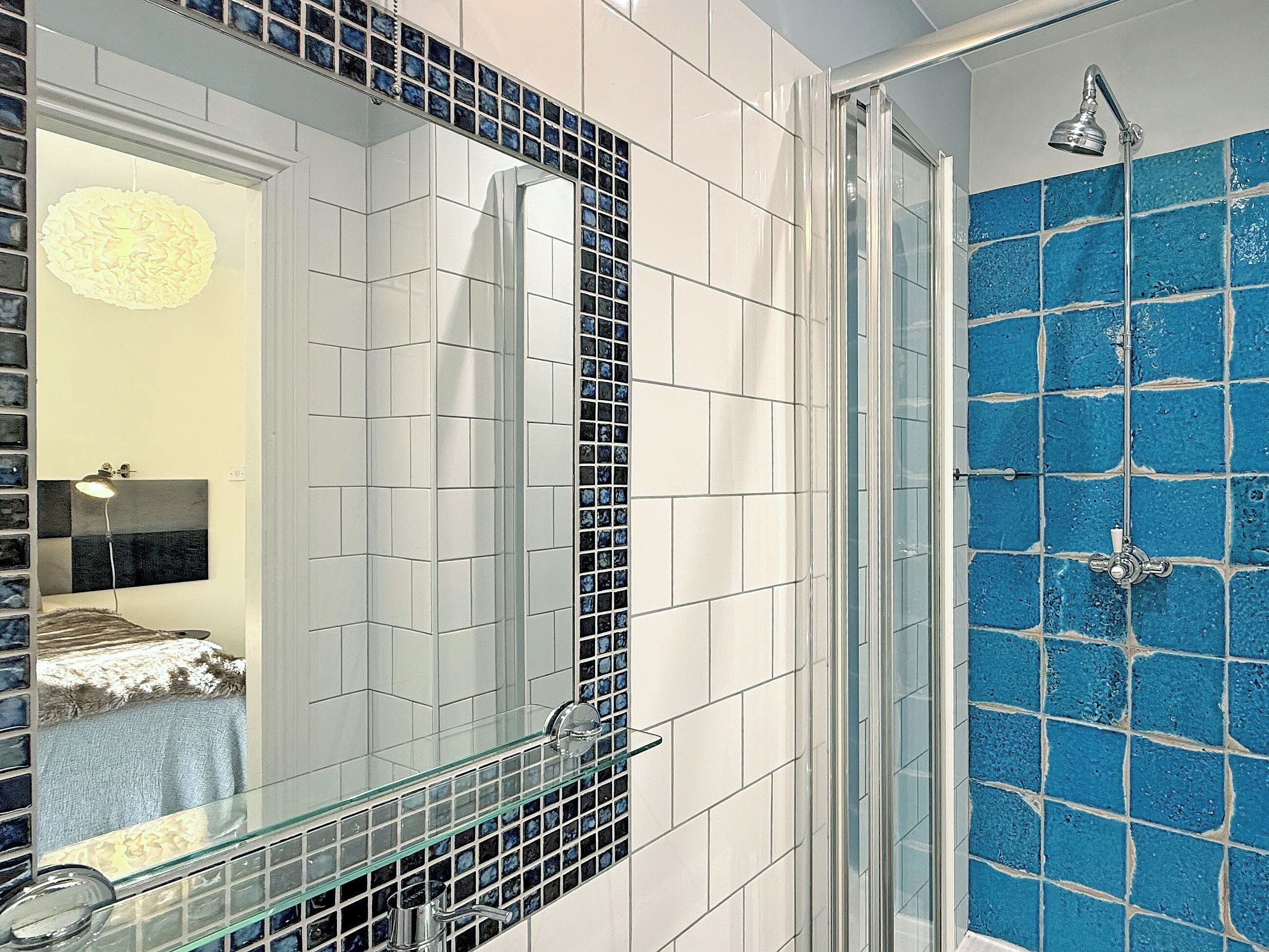 A bathroom with a glass shower enclosure, a mirror with a black frame, and a blue-tiled wall.