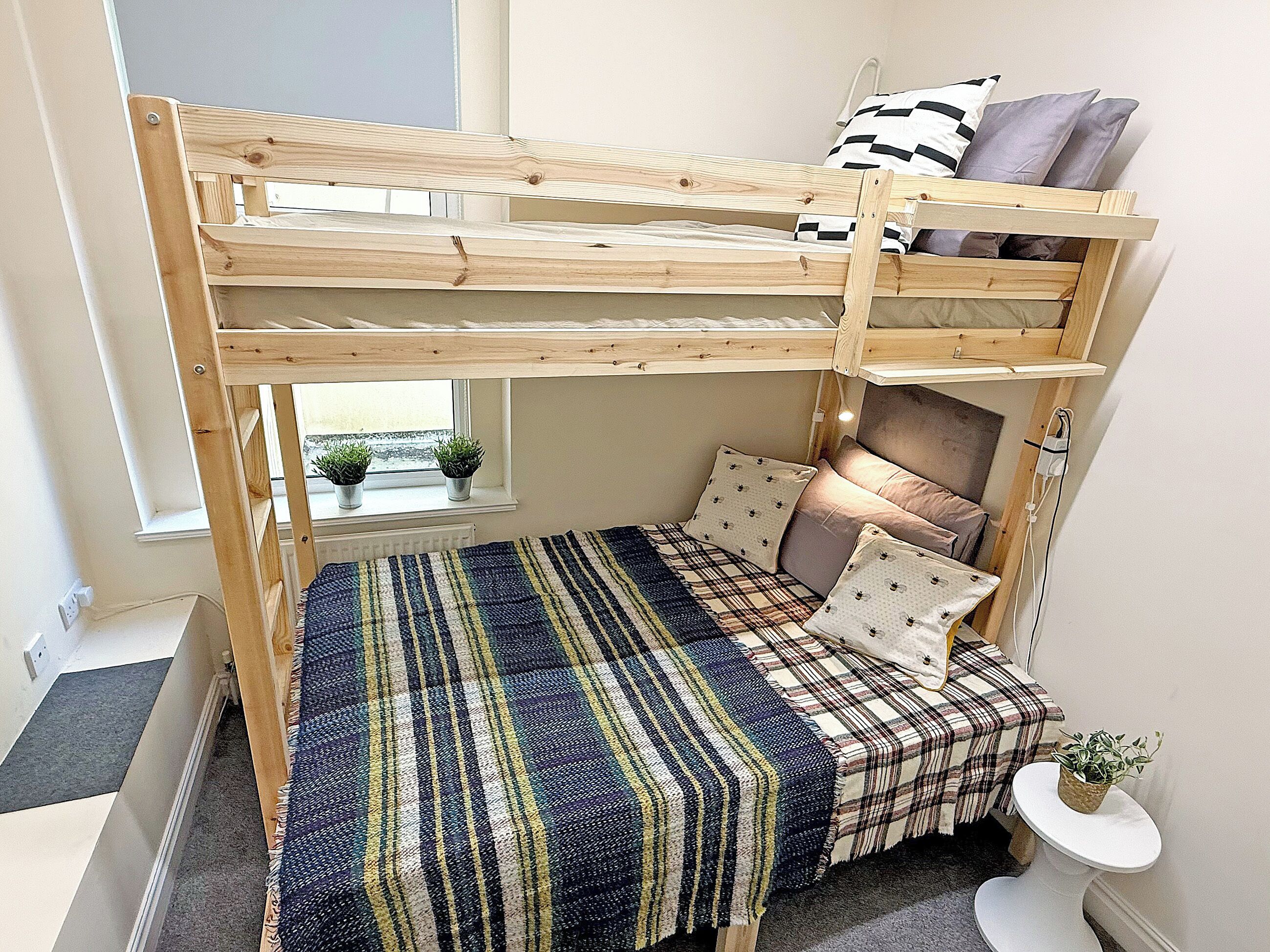 A bunk bed with a window view, a small bedside table, and a potted plant.