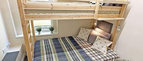 A bunk bed with a window view, a small bedside table, and a potted plant.