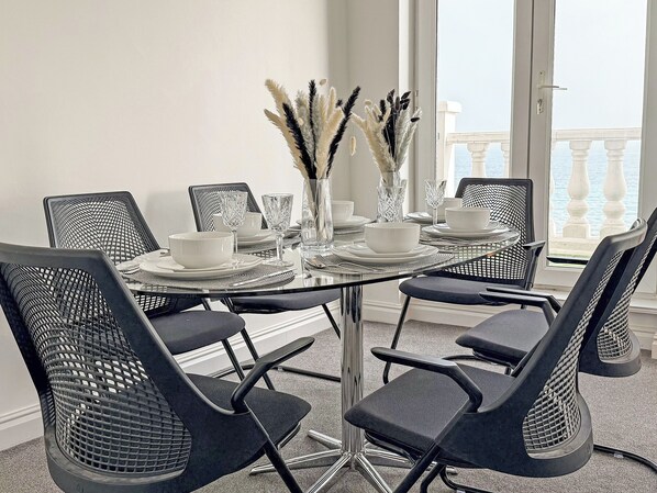 A dining area with a glass table, black mesh chairs, white plates, and clear glassware.