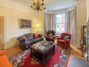A living room with a dark leather sofa, a red armchair, a patterned rug, and a chandelier.