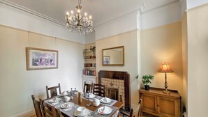 A dining room with a wooden table set for four, a chandelier, a fireplace, and a mirror on the wall.
