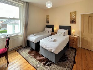 A hotel room with two beds, a wooden floor, a window with curtains, and a door.