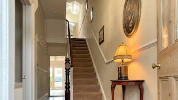 Una escalera que sube a un piso superior, una lámpara fijada a la pared y una puerta con un panel de vidrio.