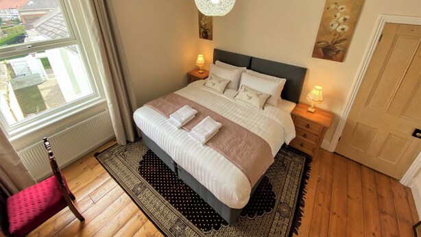 A bedroom with a bed, bedside lamps, a window, and a door.