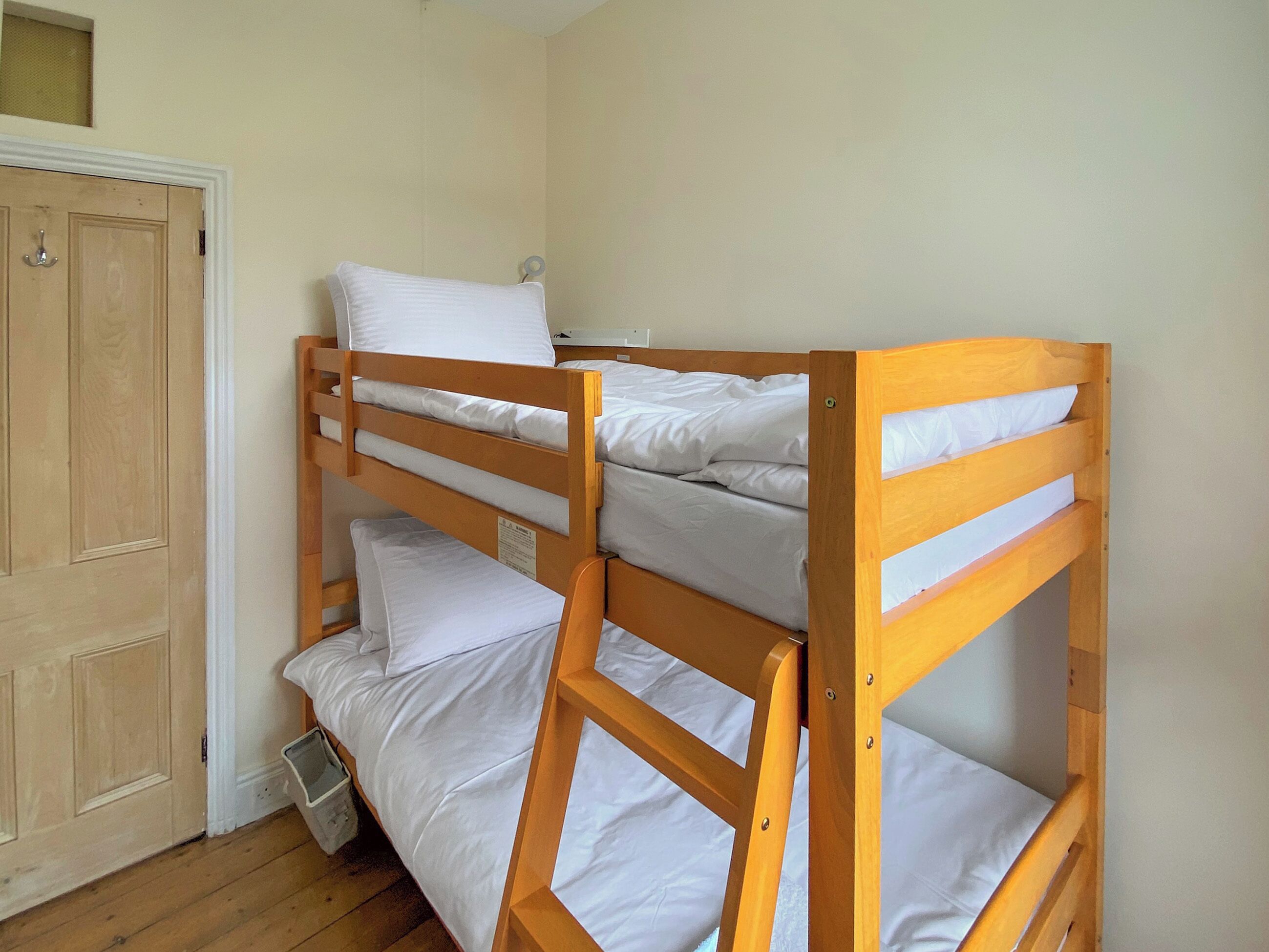 Una cama litera con ropa de cama blanca en una habitación con suelo de madera y una puerta.