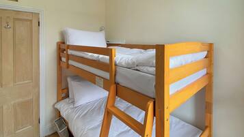 Una cama litera con ropa de cama blanca en una habitación con suelo de madera y una puerta.