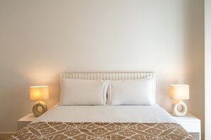 Una cama bien hecha con un edredón estampado, dos lámparas de noche y un cabecero sencillo.