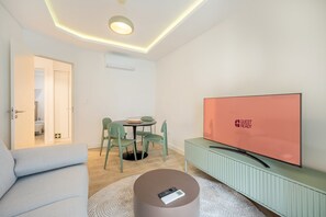 A modern living room with a sofa, a dining table with chairs, a television, and a small round table with a remote control. - GuestReady – Romantic Lisbon Nook (Lisbon)