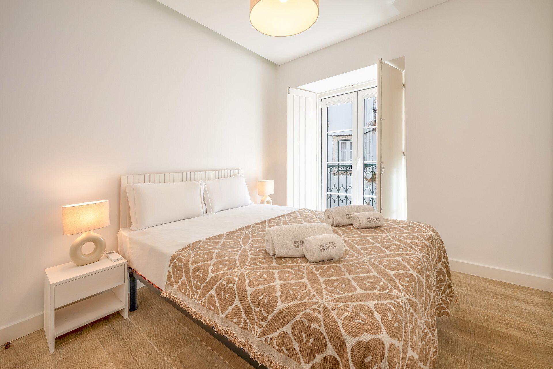A hotel room with a bed, bedside lamps, a nightstand, and a view of the outside balcony.