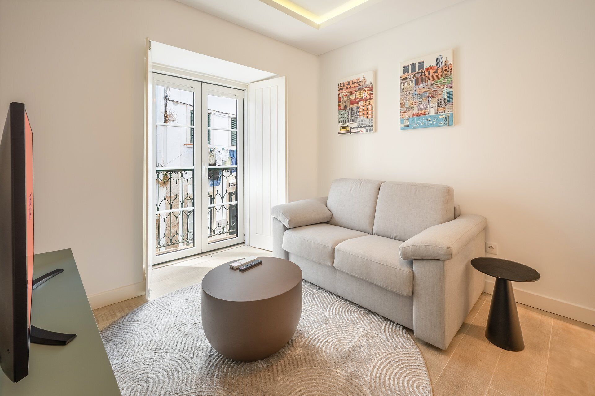 Un salon moderne avec un canapé, un pouf rond, une petite table et un téléviseur.