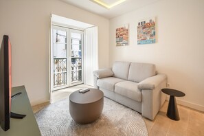 A modern living room with a sofa, a round ottoman, a small table, and a TV. - GuestReady – Romantic Lisbon Nook (Lisbon)
