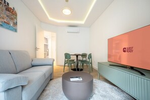 Una sala moderna con un sofá gris, una mesa redonda, un televisor de pantalla plana y un área de comedor con mesa y sillas.