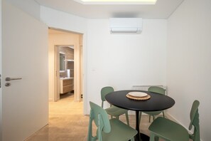 Una habitación con una mesa redonda, cuatro sillas, un aire acondicionado instalado en el techo y una puerta que da a un pasillo.