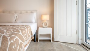 A hotel room with a bed, a bedside table with a lamp, and a door leading to an outdoor area. - GuestReady – Romantic Lisbon Nook (Lisbon)