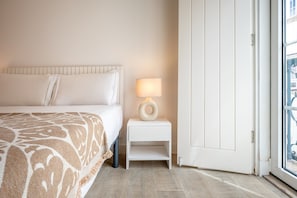 A hotel room with a bed, a bedside table with a lamp, and a door leading to an outdoor area. - GuestReady – Romantic Lisbon Nook (Lisbon)