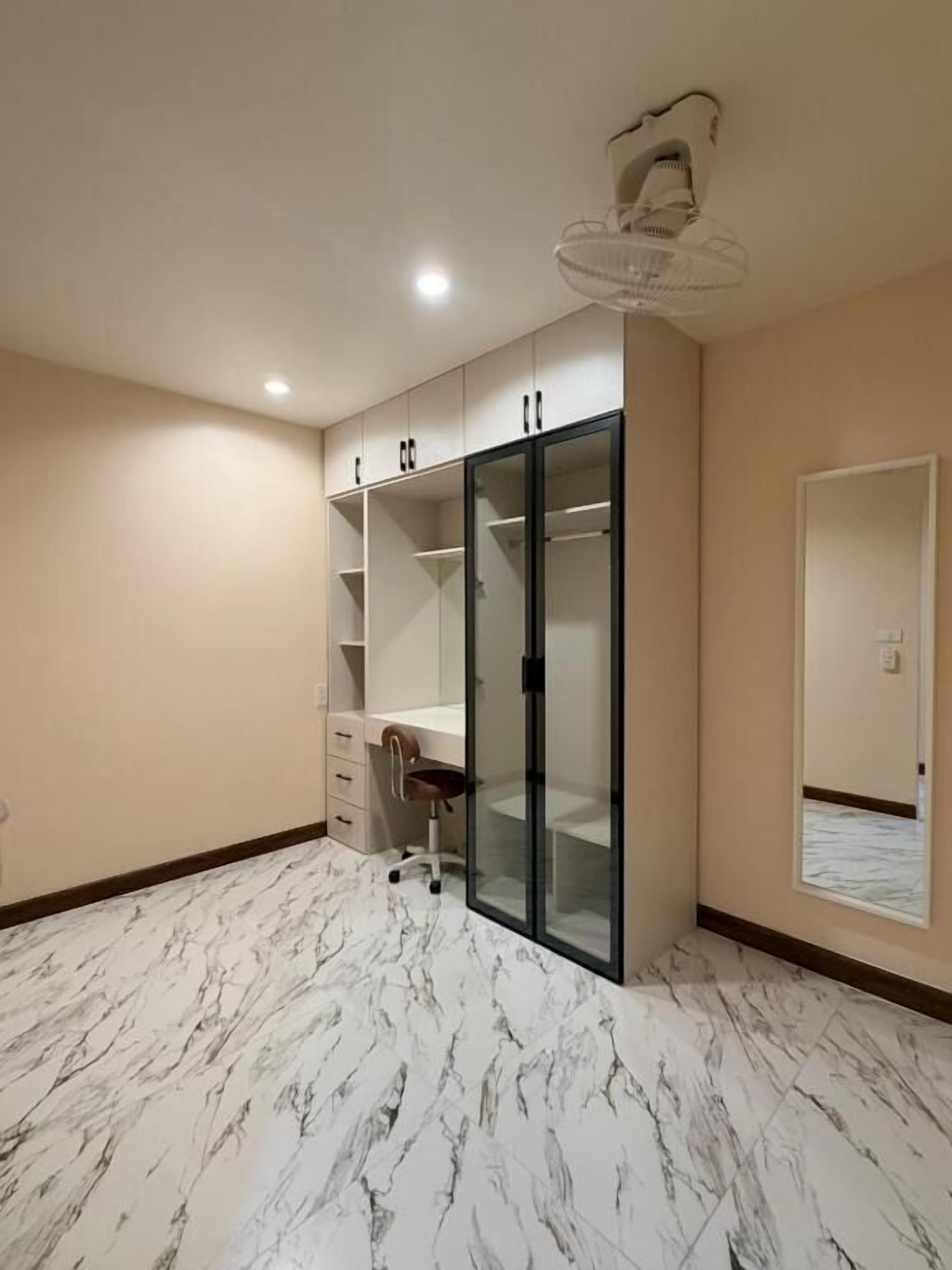 A room with a marble floor, a desk, a chair, a wardrobe with glass doors, and a ceiling fan.