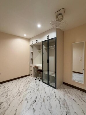 Habitación con piso de mármol, un escritorio, una silla, un armario con puertas de vidrio y un ventilador de techo.