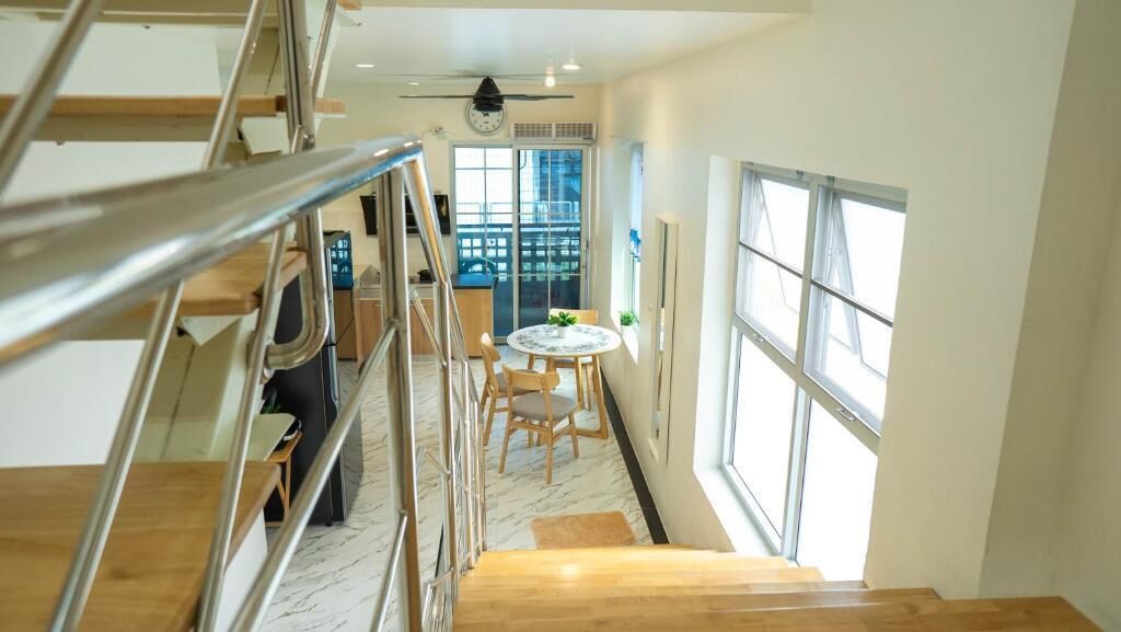Un escalier menant à une salle à manger avec une table ronde et des chaises, une vue sur l’extérieur par une fenêtre et un ventilateur de plafond.