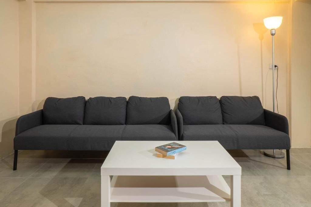 A room with two dark-colored sofas, a white coffee table with a book, and a floor lamp.