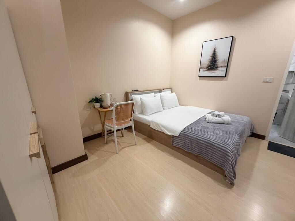 A bedroom with a bed, a chair, a bedside table, and a wall-mounted picture.